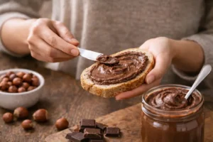 žena natiera domácu nutellu na krajec chleba, domáca nutella, zdravá nutella, recept na domácu nutellu, domáca nutella recept, oriešková pomazánka recept, kakaovo oriešková pomazánka recept, vegan nutella, fit nutella